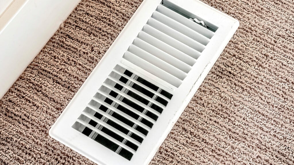 Panorama White air conditioner duct grille cover against floor with brown carpet. The cover has adjustable linear slots to direct air flow inside the room.